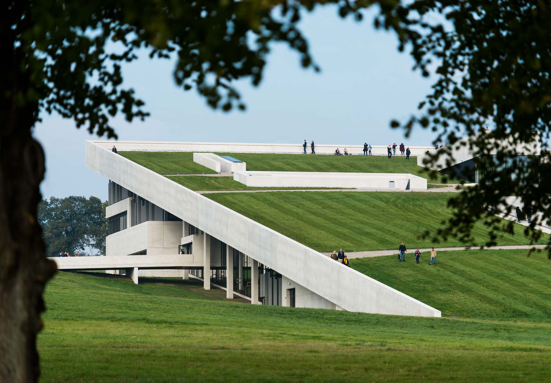 A modern building with a unique architectural design featuring a sloped, grass-covered roof that extends to the ground, allowing access to the rooftop. This design blends the structure into the landscape.