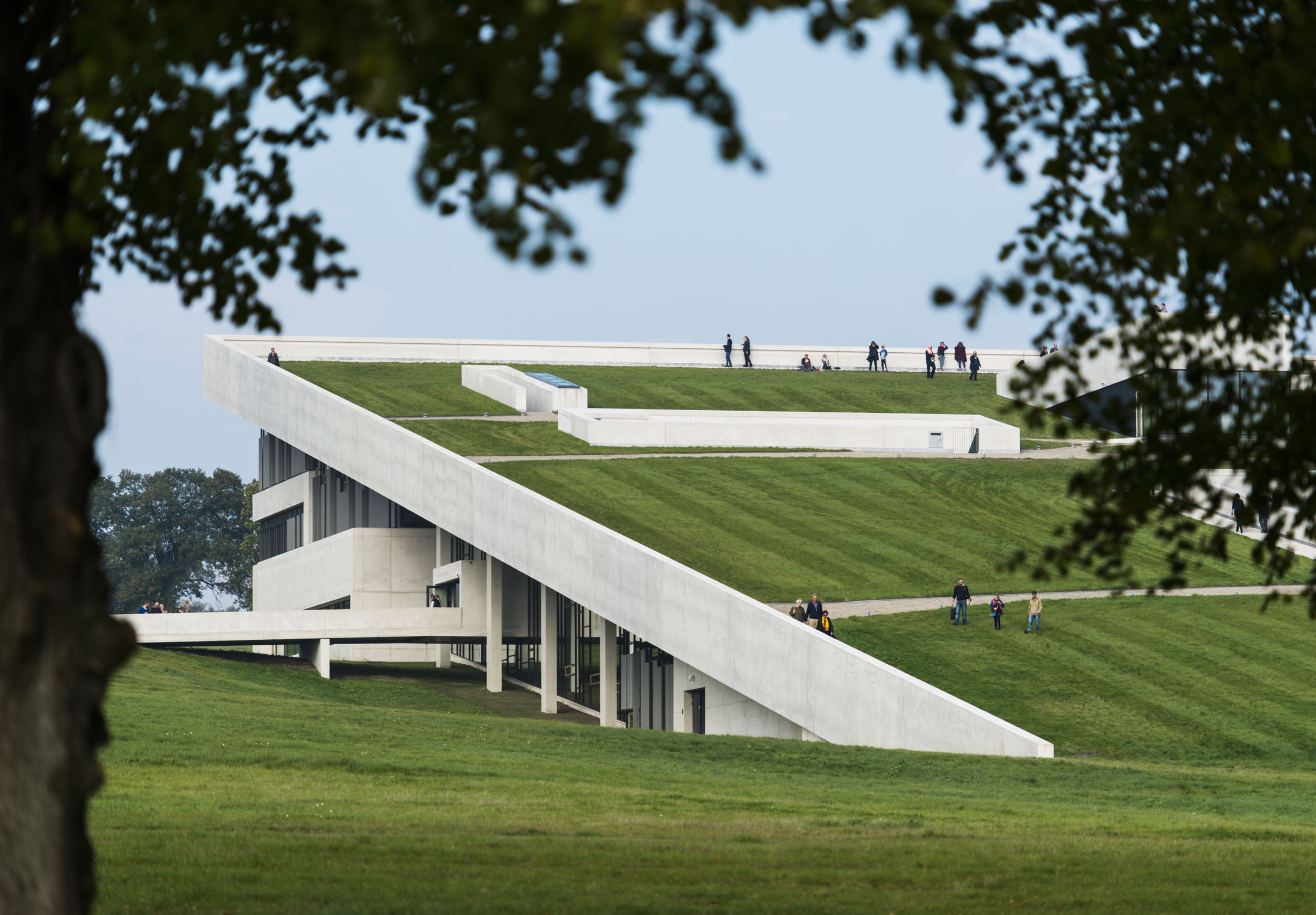 A modern building with a unique architectural design featuring a sloped, grass-covered roof that extends to the ground, allowing access to the rooftop. This design blends the structure into the landscape.